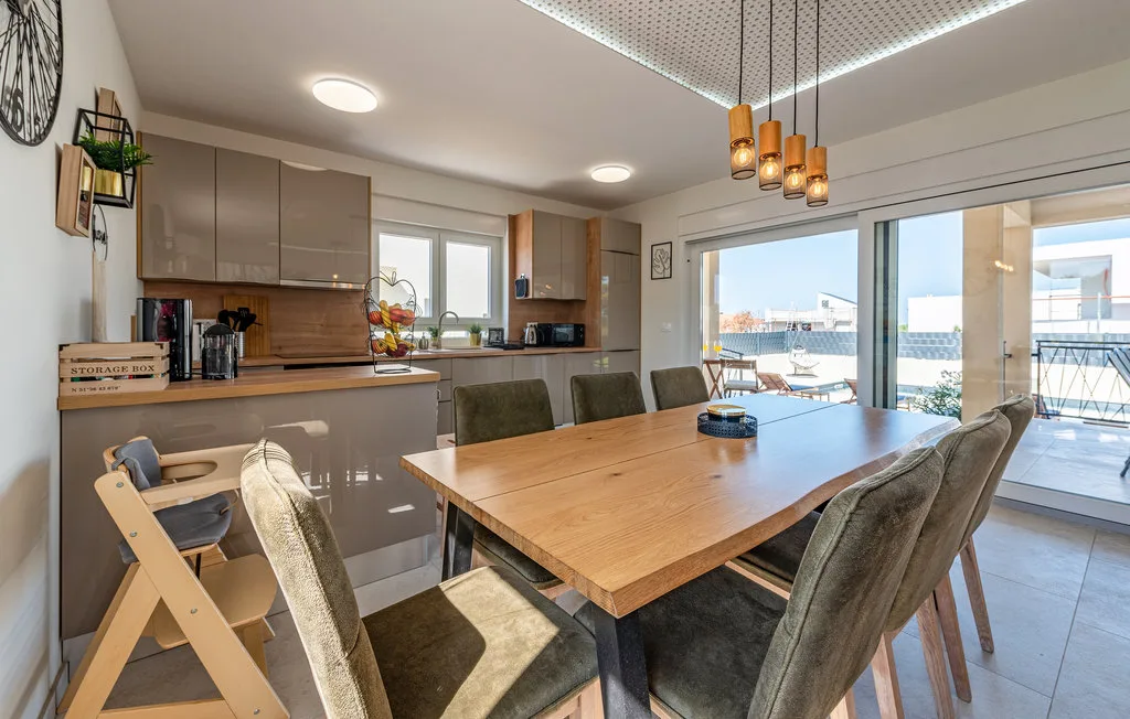 Comedor con una mesa grande de madera junto a una cocina abierta y puertas de vidrio.