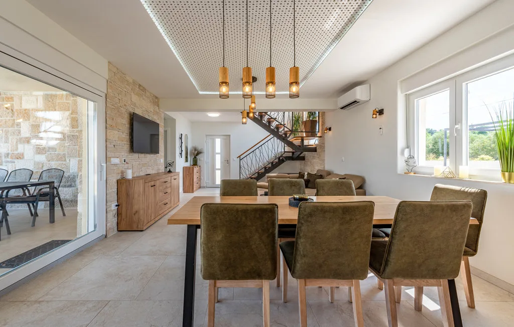 Comedor con una mesa larga y sillas, junto a una sala de estar y una escalera.
