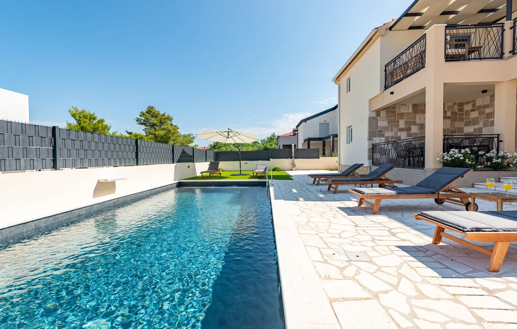 An outdoor swimming pool beside a sunny patio with lounge seating.