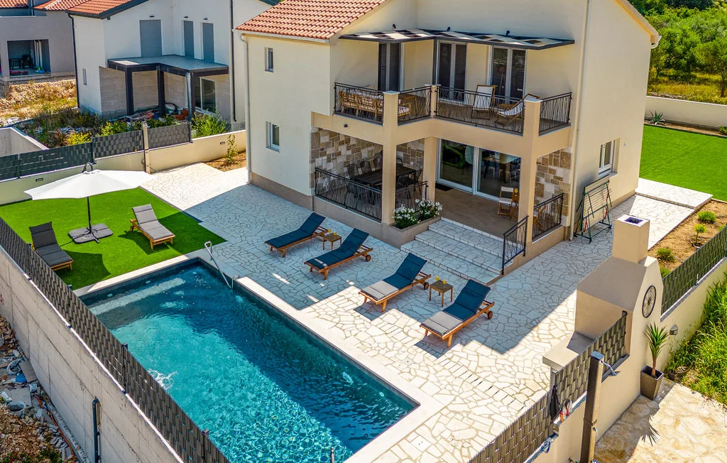 A villa and outdoor pool are surrounded by a paved patio with seating.