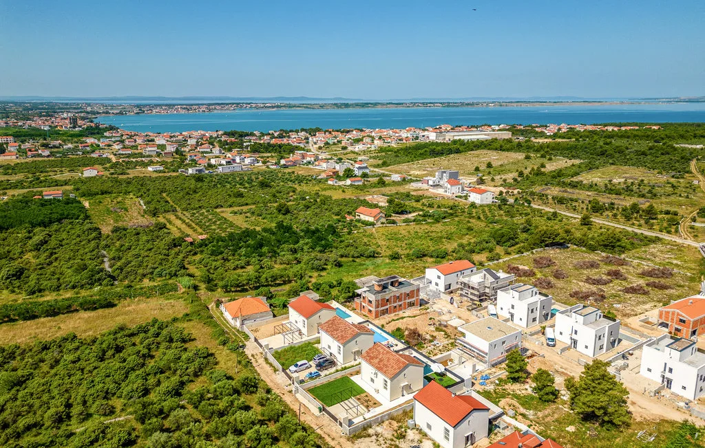 Aerial view of a residential area with homes, green fields, and water in the distance.