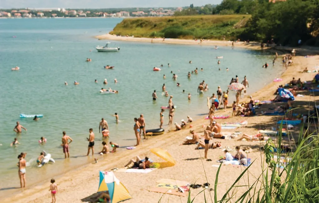 A busy beach scene with swimmers in the water and people relaxing on the sand.