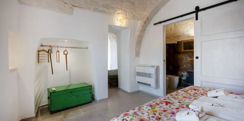 A bedroom with a green storage chest, wall hooks, and an open bathroom doorway.