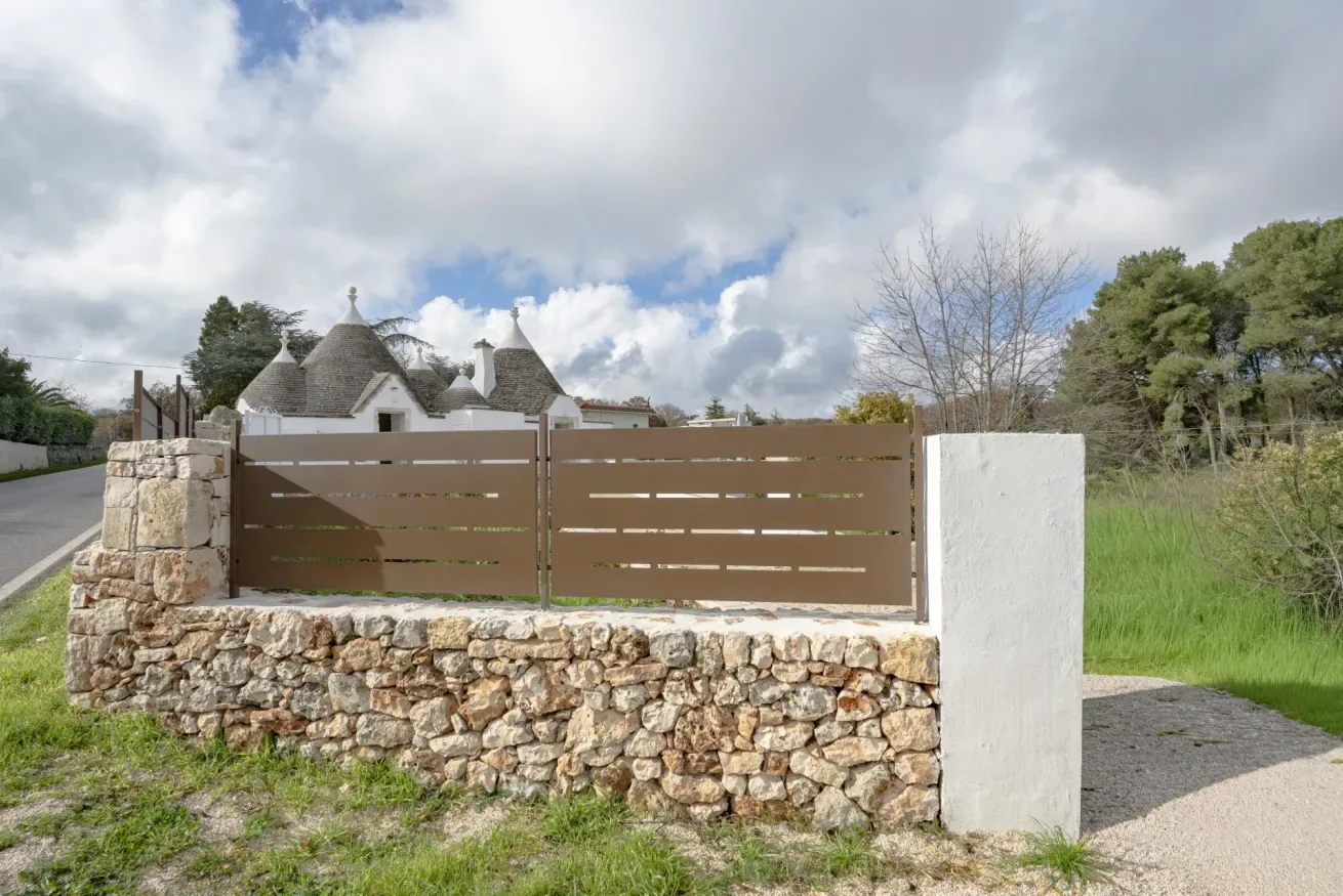A brown gate and stone wall stand in front of white buildings with conical roofs.