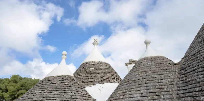 A cluster of conical stone rooftops stands beneath a partly cloudy sky.