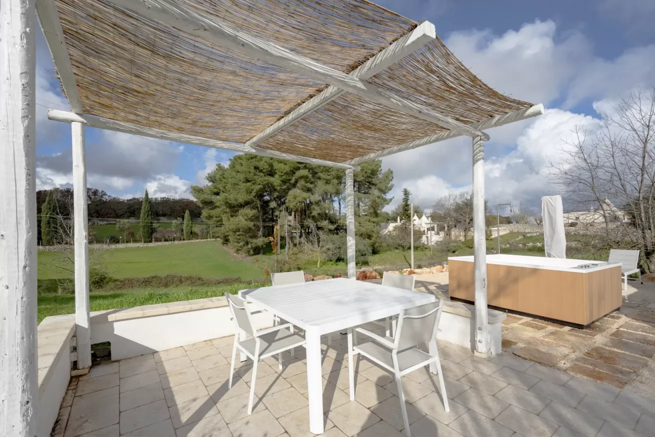 An outdoor patio dining area beneath a woven shade canopy, with a hot tub nearby.