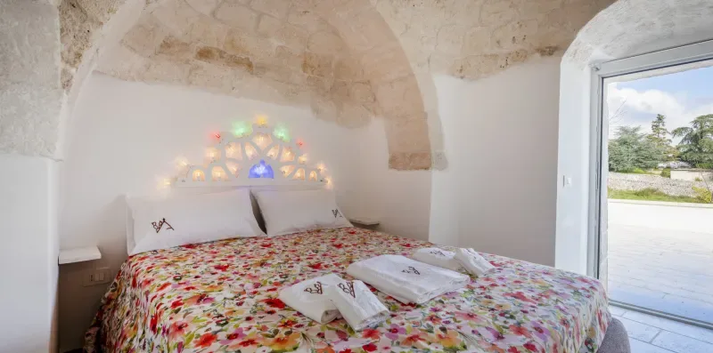 A bedroom with a floral bedspread and colorful lights above the bed.