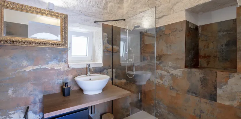 A bathroom with a vessel sink, wall mirror, and glass shower screen.
