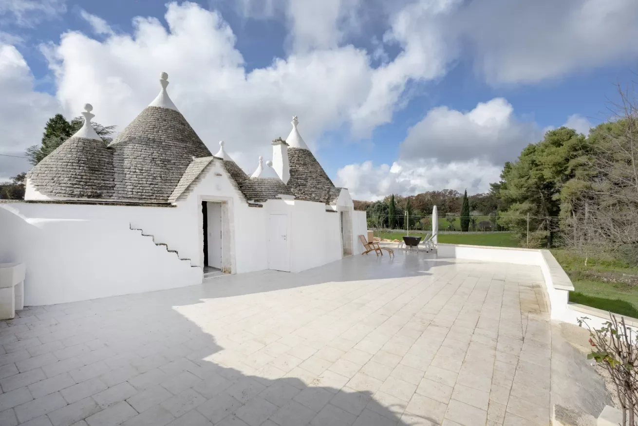 A white building with conical roofs opens onto a broad paved terrace.