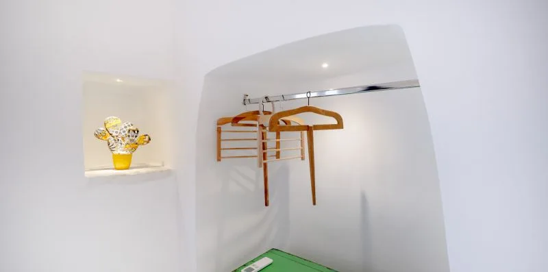 A recessed clothing area has a metal rail with wooden hangers.