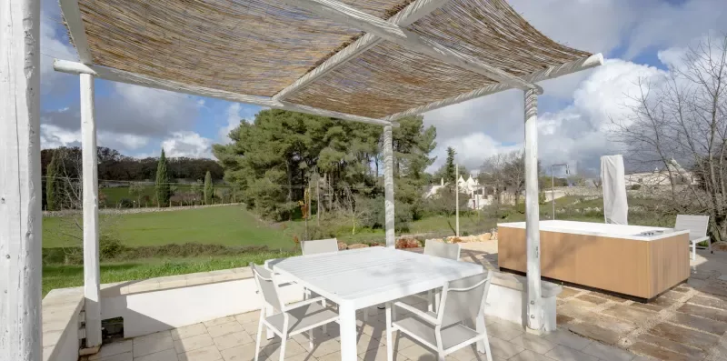 A patio dining area under a woven shade canopy overlooks a green lawn.