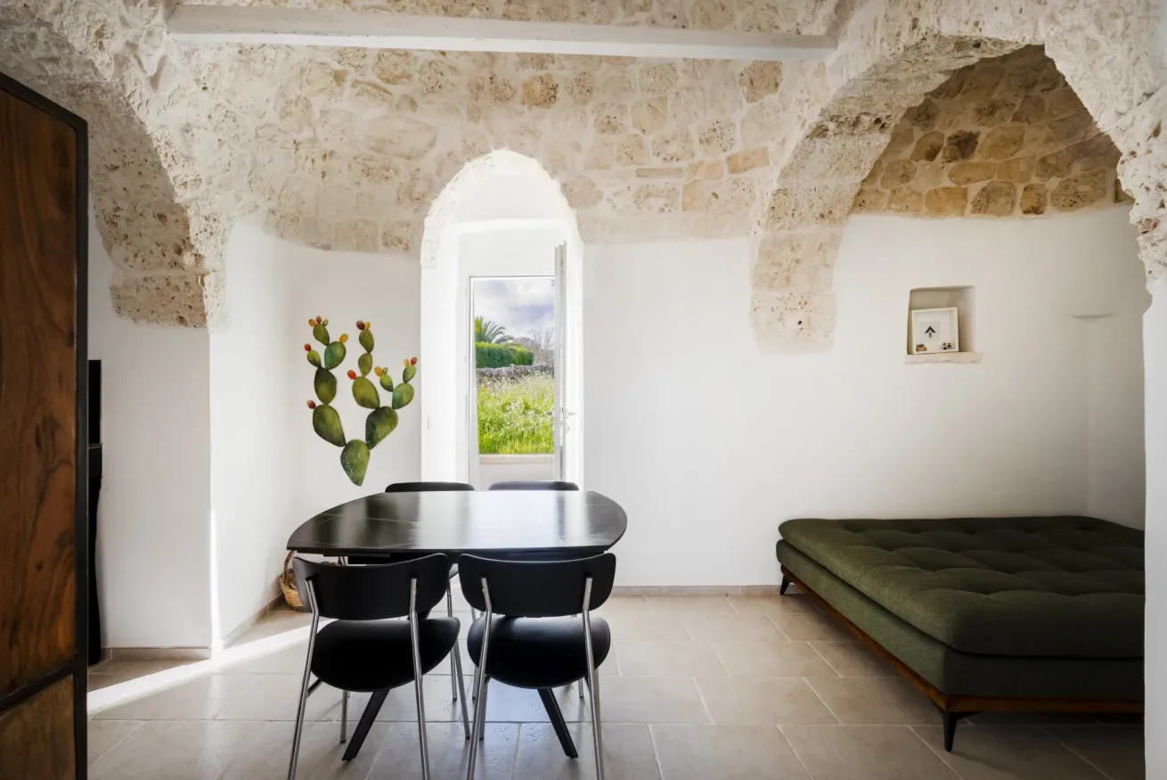 A stone-walled dining area has a table beside a window and a green daybed.