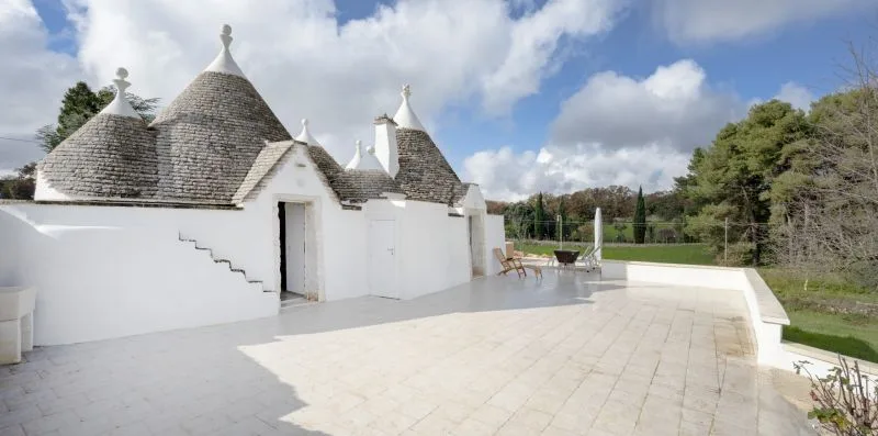 A pale stone terrace beside white buildings with conical roofs, overlooking green grounds.