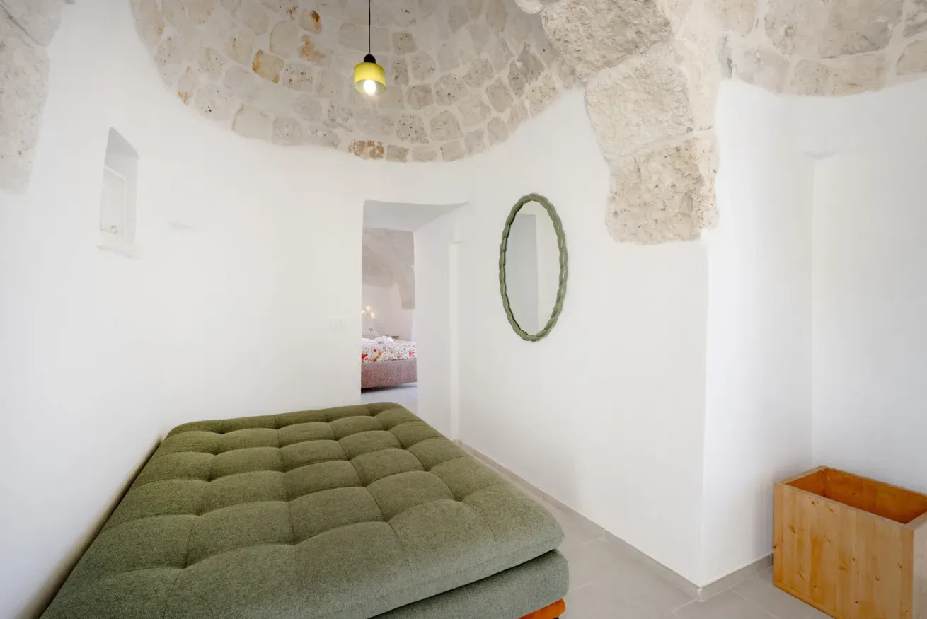 A bedroom with a low green bed beneath a vaulted stone ceiling.