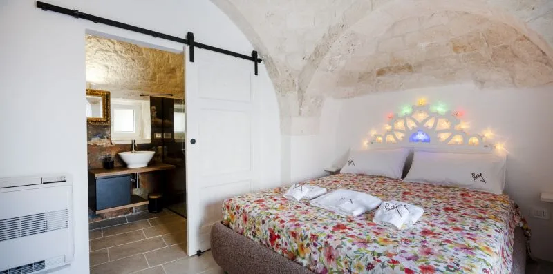 A bedroom with a colorful patterned bedspread beneath a curved stone ceiling.