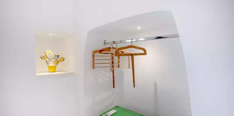 A recessed closet area has a hanging rail with wooden hangers and a small shelf.