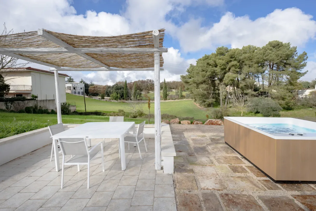 An outdoor patio with a dining table under a pergola beside a pool.