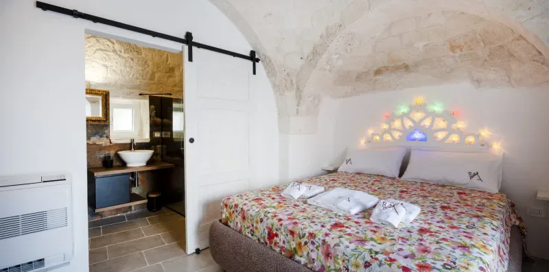 A bedroom with a floral bedspread beside an open bathroom doorway.