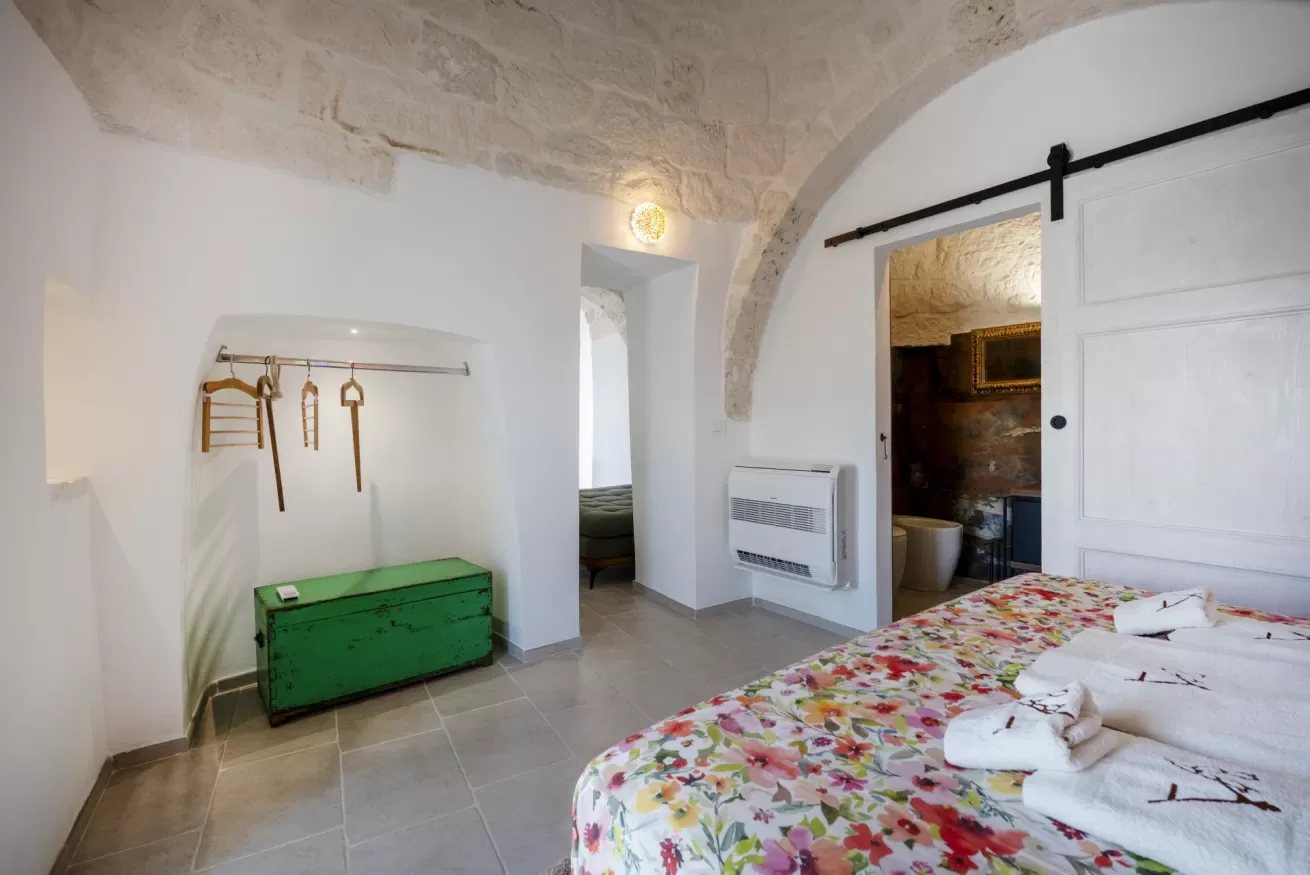 A bedroom with a floral bedspread and a green chest beneath a wall rack.