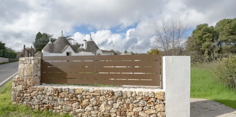 A brown gate and stone wall stand beside a grassy roadside.