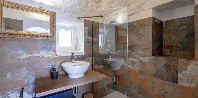 A bathroom with a sink, wall mirror, and glass shower screen.