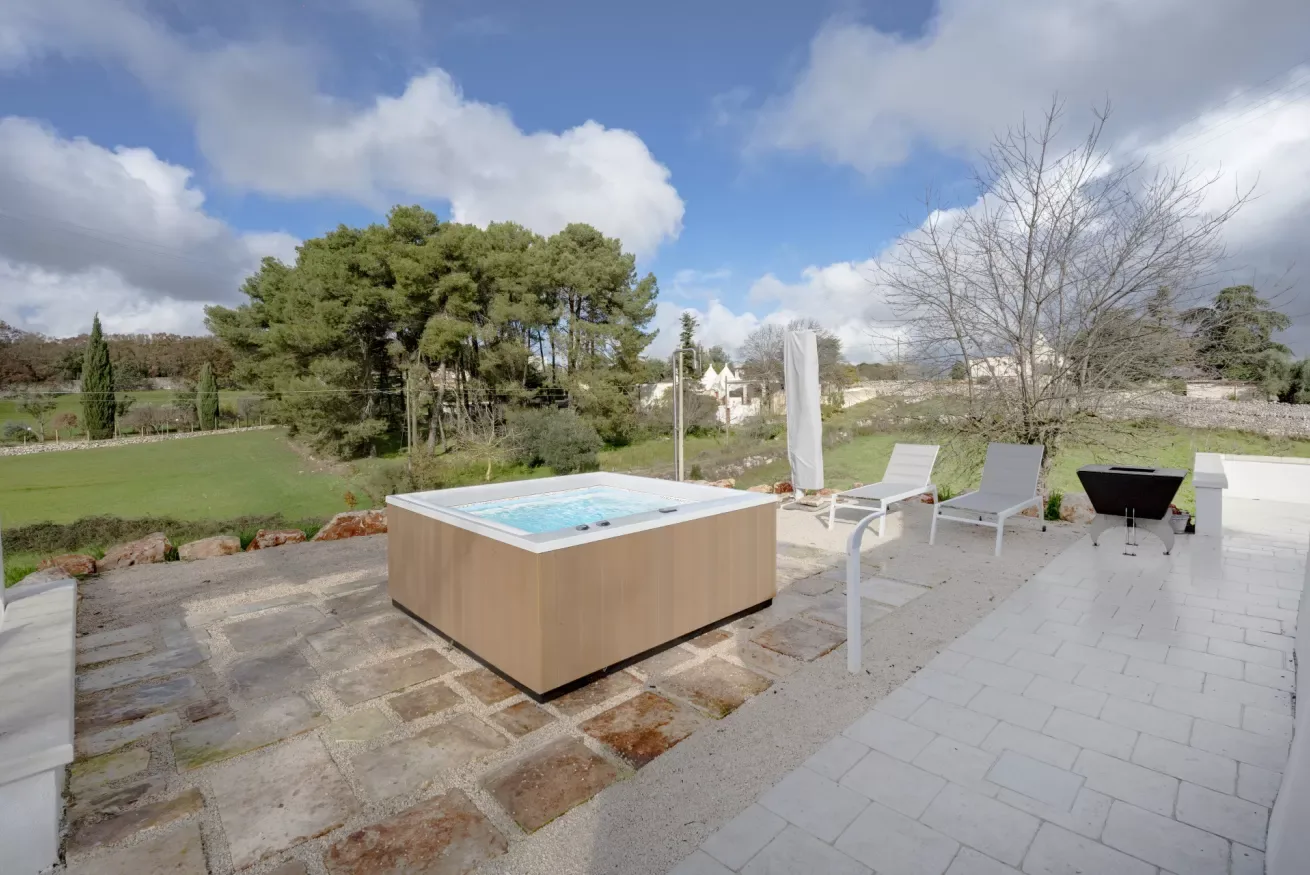 An outdoor patio features a square hot tub, lounge seating, and open countryside views.