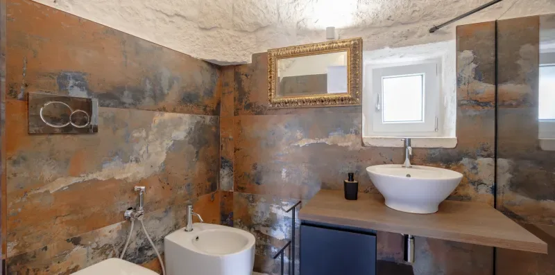 A bathroom with a wall-mounted sink, countertop, and small window.
