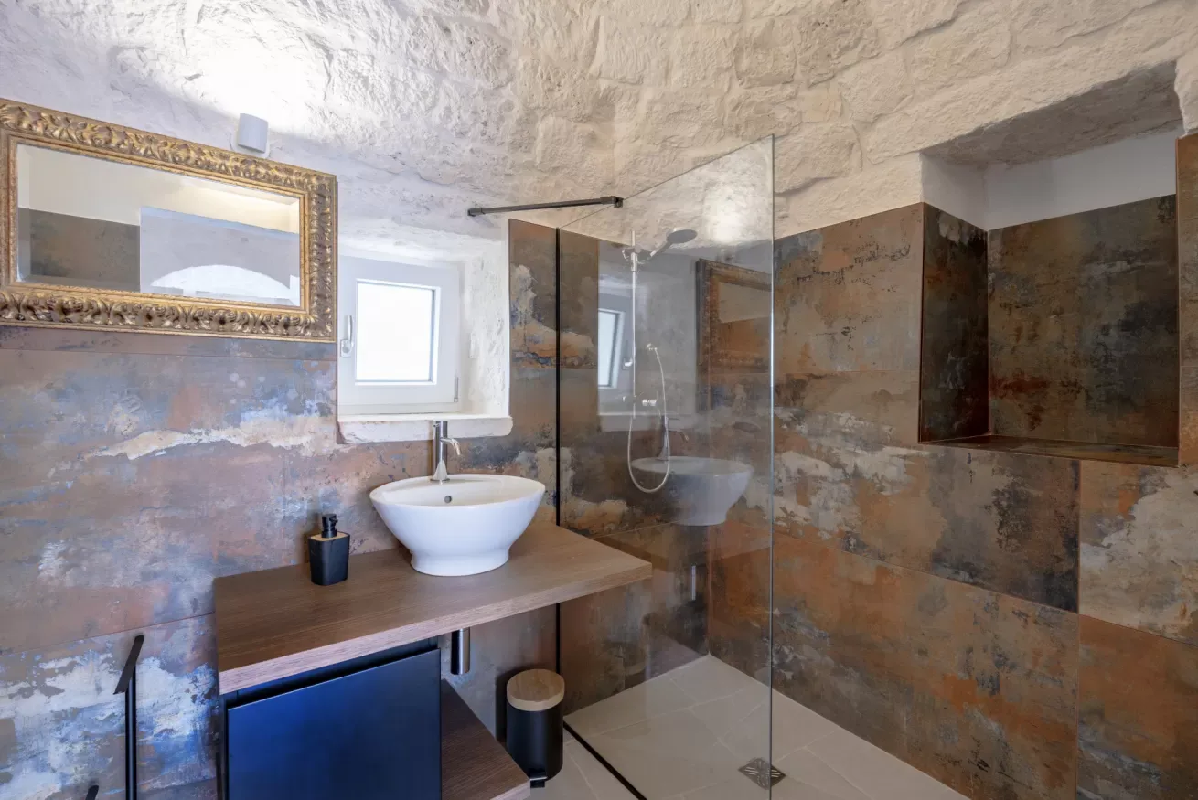 A bathroom with a vessel sink, wall mirror, and glass shower screen.