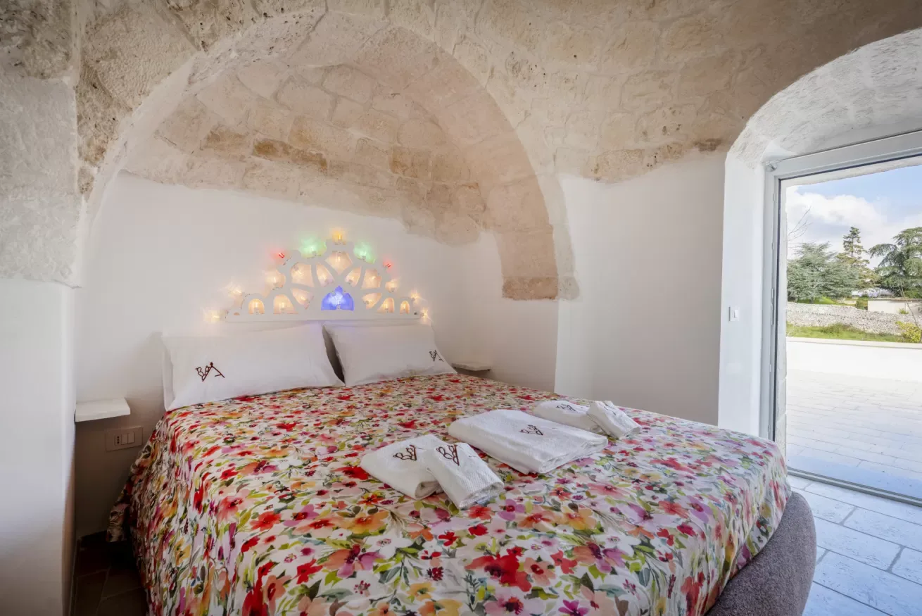 A bedroom with a flower-patterned bedspread and a small arched window.