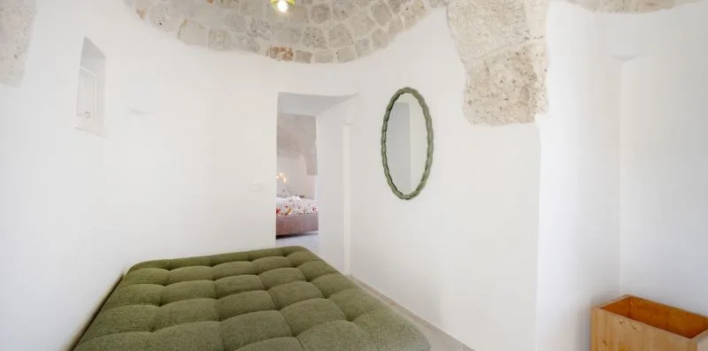 A bedroom with a green bed and an oval mirror on the wall.