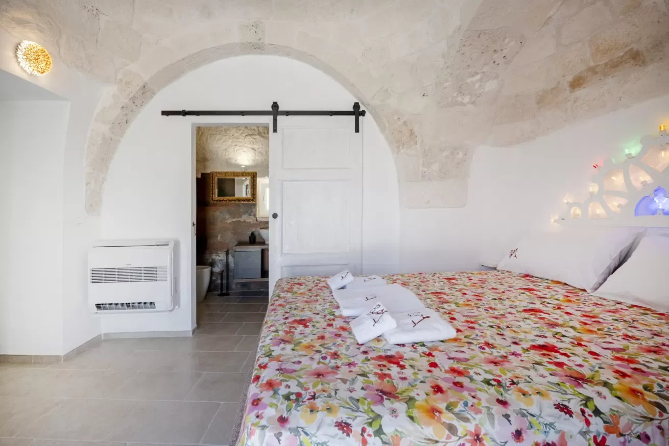 A bedroom with a floral bedspread beneath a broad stone arch.