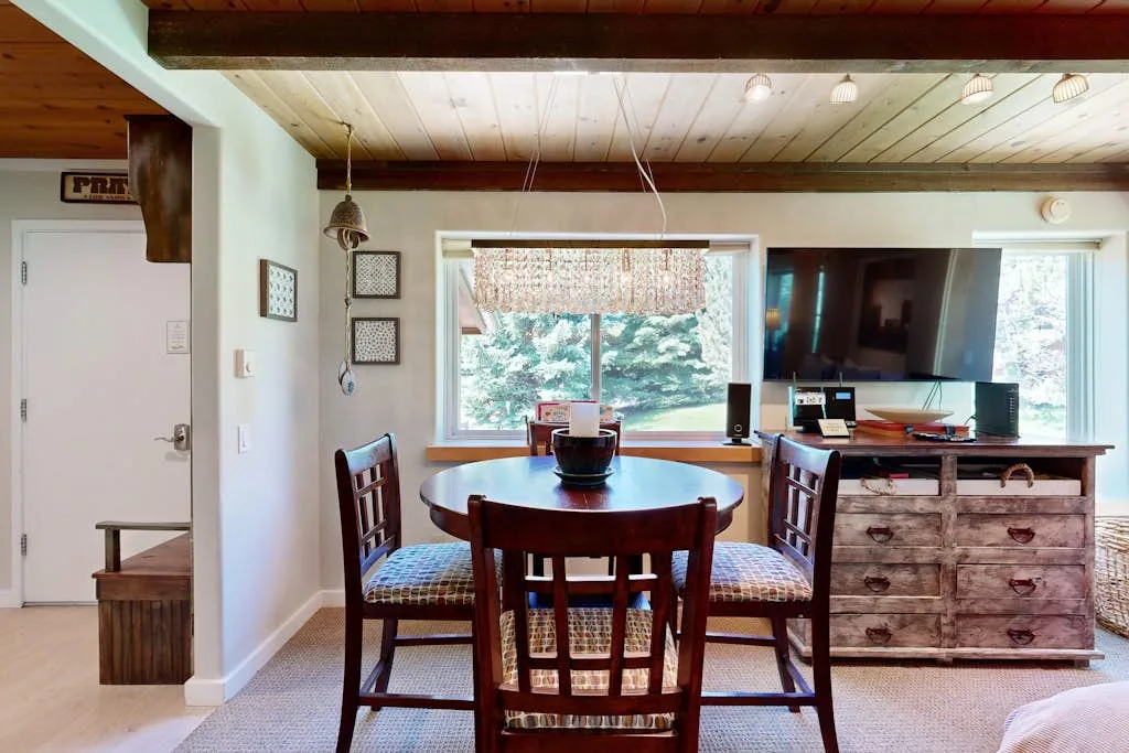 A dining area with a wooden table and chairs beside a large window.