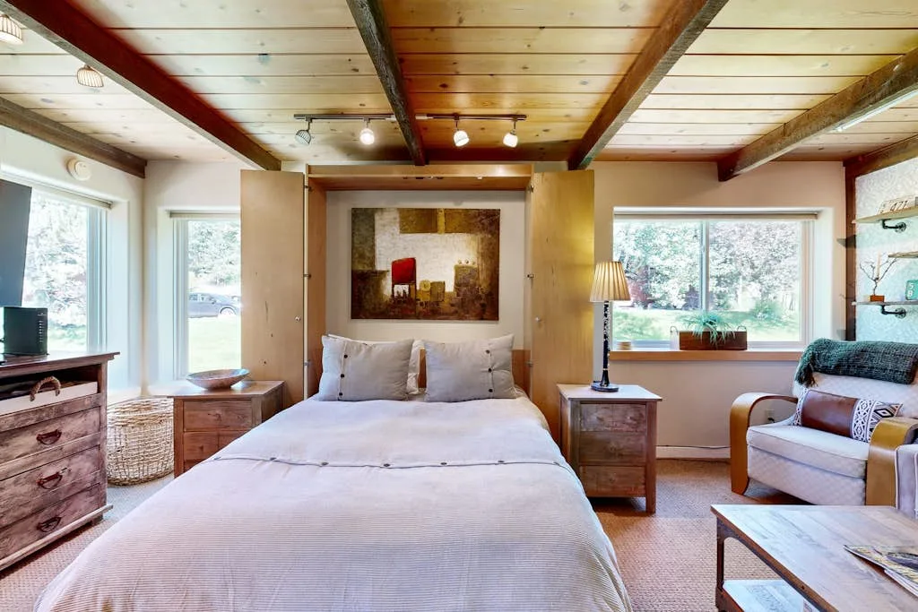 Un dormitorio con una cama grande, mesitas de noche y ventanas.