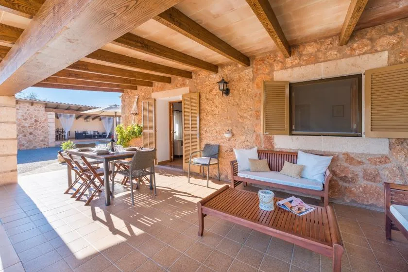 A covered stone patio with outdoor seating and a dining table.
