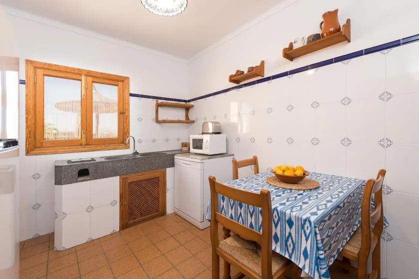 A tiled kitchen with a wooden table covered by a blue patterned cloth.