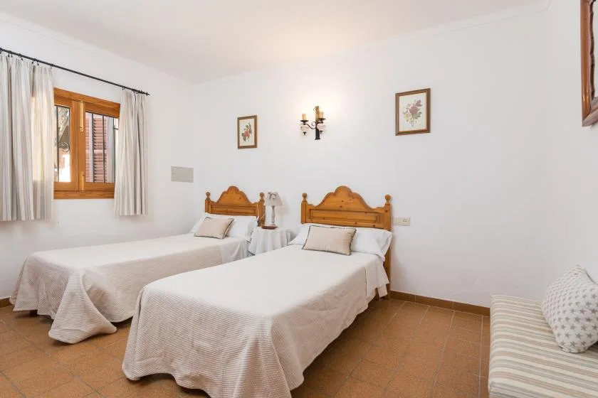 A bedroom with two single beds, a curtained window, and a small seating area.