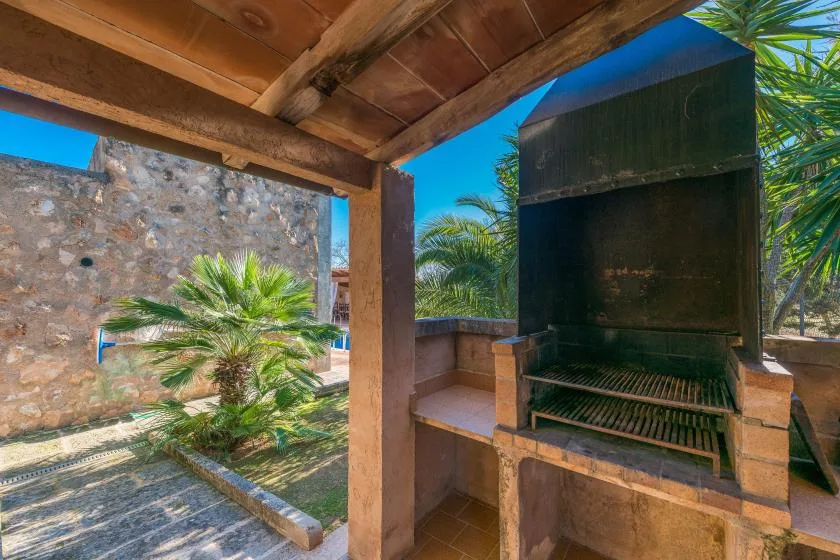 A covered outdoor barbecue area with a large built-in grill and tropical plants.