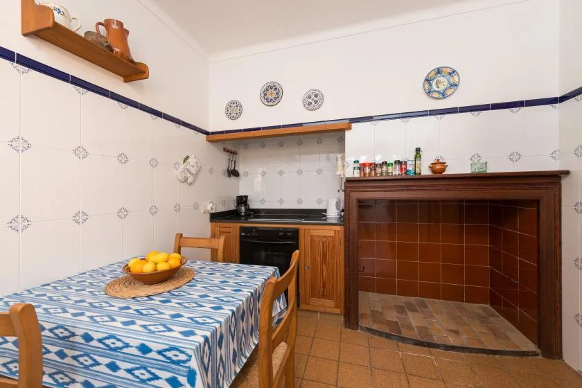 A tiled kitchen and dining area with a table set beside a large brick hearth.