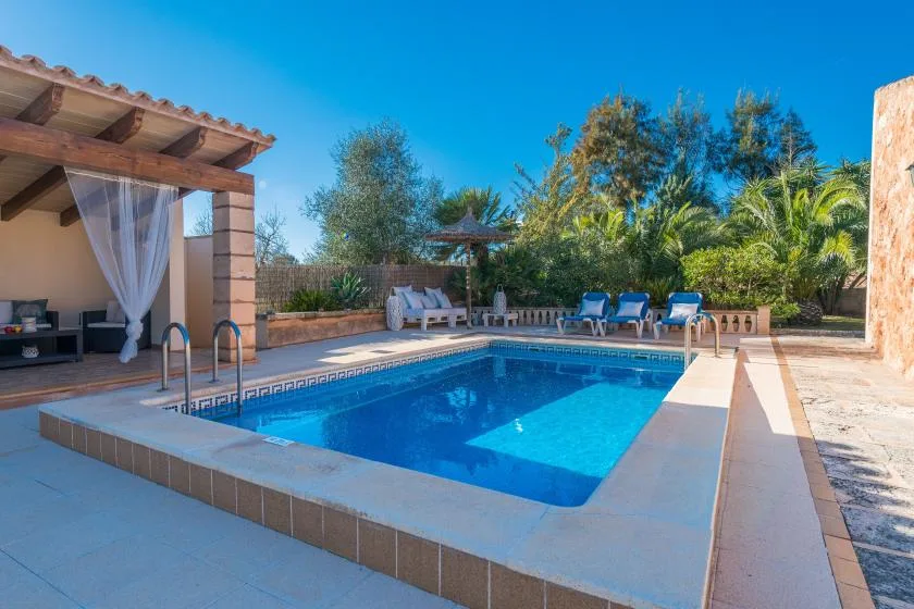 A backyard swimming pool is surrounded by lounge seating and greenery.