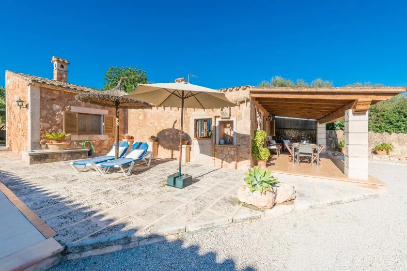 A sunny stone patio has lounge seating, an umbrella, and a covered dining area.