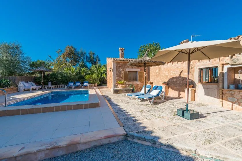 A sunlit poolside patio with lounge seating and a large shade umbrella.