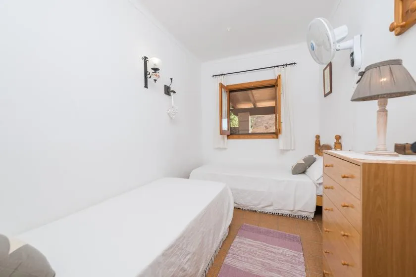 A bright bedroom with two beds, a window, and a wooden dresser.