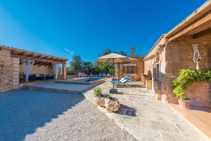 A stone courtyard with a swimming pool, shaded seating, and a patio umbrella.