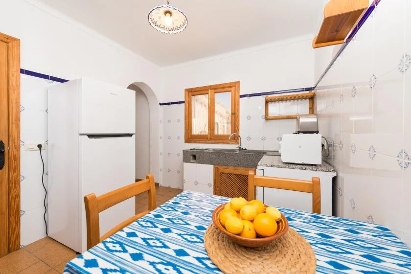 A kitchen dining area with a blue patterned tablecloth and a bowl of oranges.