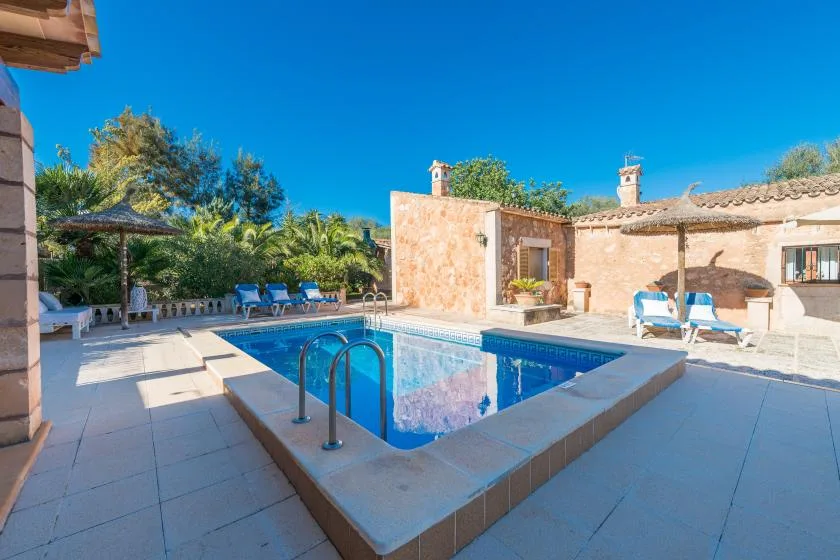 A sunny outdoor pool sits beside a stone building and patio seating.