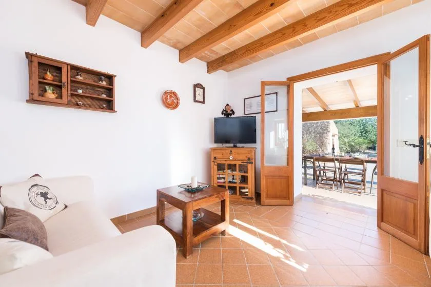 A living room with seating, a television, and open wooden doors leading to a patio.