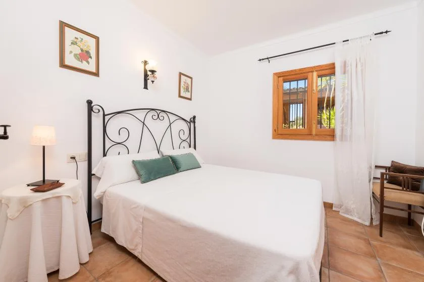 A bright bedroom with a neatly made bed and a wood-framed window.