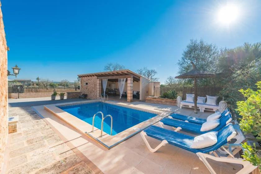 An outdoor swimming pool sits beside a covered patio and lounge seating.
