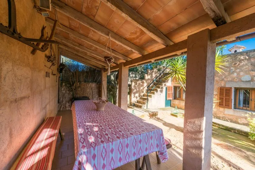 A covered outdoor dining area with a patterned tablecloth and wooden benches.
