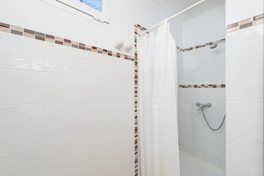A tiled bathroom with a shower and white curtain.